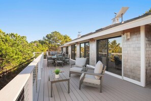 Une terrasse extérieure moderne dotée d’un espace repas, de sièges et offrant une vue sur les arbres environnants.