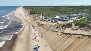 Vue aérienne d’une plage avec un parking, des bâtiments et une falaise.