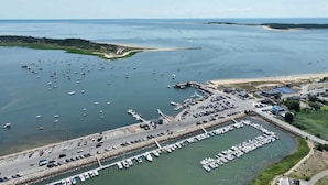 Vue aérienne d’une marina où sont amarrés de nombreux bateaux, avec un espace de stationnement et une route menant à la marina.