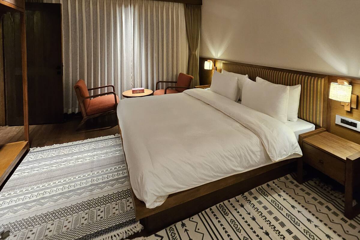 Une chambre d’hôtel avec un grand lit, deux chaises, une petite table et une table de chevet avec une lampe.