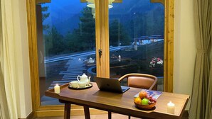 Une table à manger avec un ordinateur portable, une bougie, un plateau avec une théière et des tasses, et un saladier rempli de fruits.