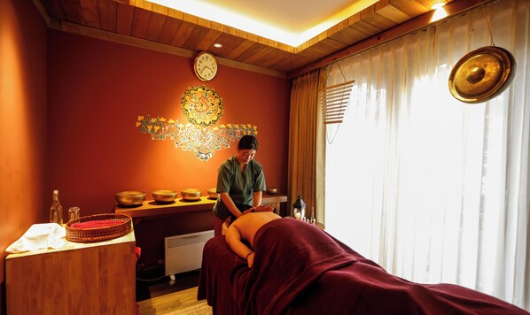 Une salle de massage avec un plafond en bois, une horloge murale, un élément décoratif mural, une table de massage et une fenêtre avec des rideaux.