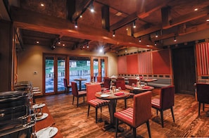 A restaurant with wooden floors, red upholstered chairs, and a view of a water body through glass doors.