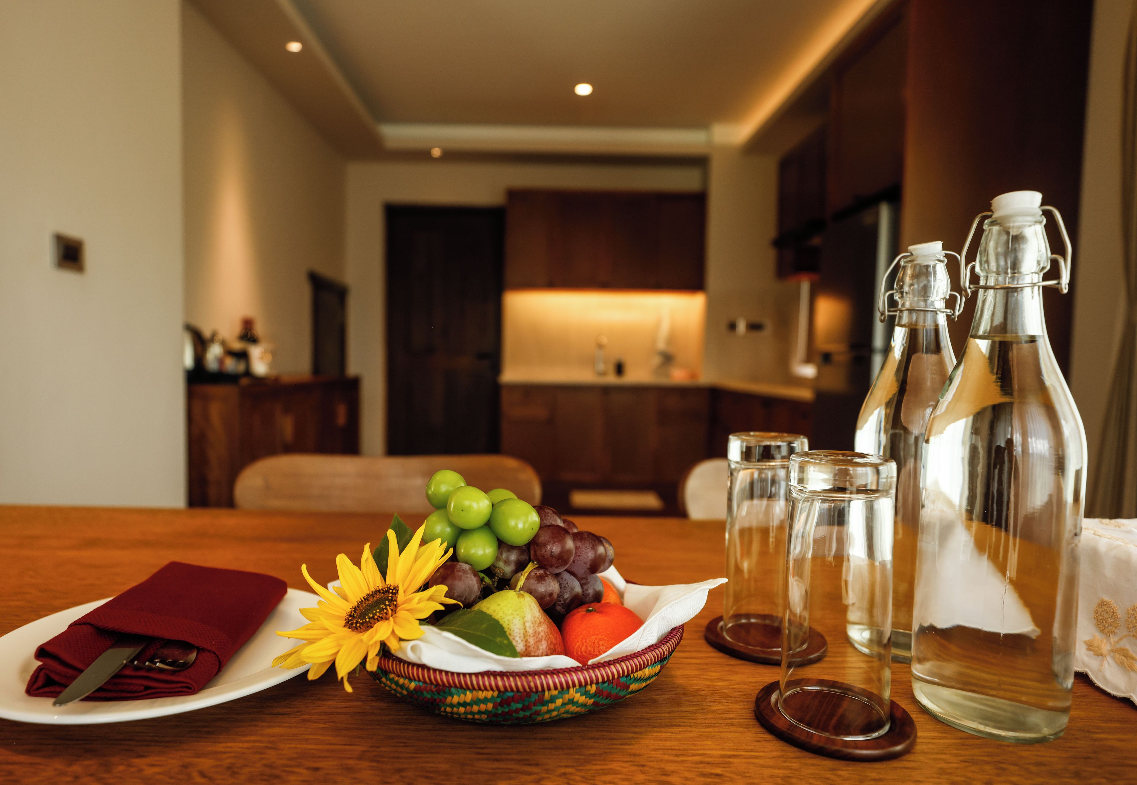 Una mesa de comedor con una cesta de frutas, una servilleta y dos botellas de vidrio.