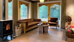 Un salon chaleureux avec une cheminée, un canapé, un fauteuil, une table basse avec des fruits et de grandes fenêtres avec des rideaux.