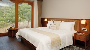 Une chambre spacieuse avec un grand lit, une tête de lit en bois et une vue sur les arbres, visible à travers une porte-fenêtre coulissante.