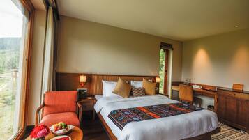 A hotel room with a bed, a chair, a nightstand, a desk, and a view of the outdoors.
