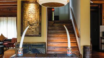 A room with a wooden ceiling, a large decorative wall piece, a staircase, and a unique floor lamp.