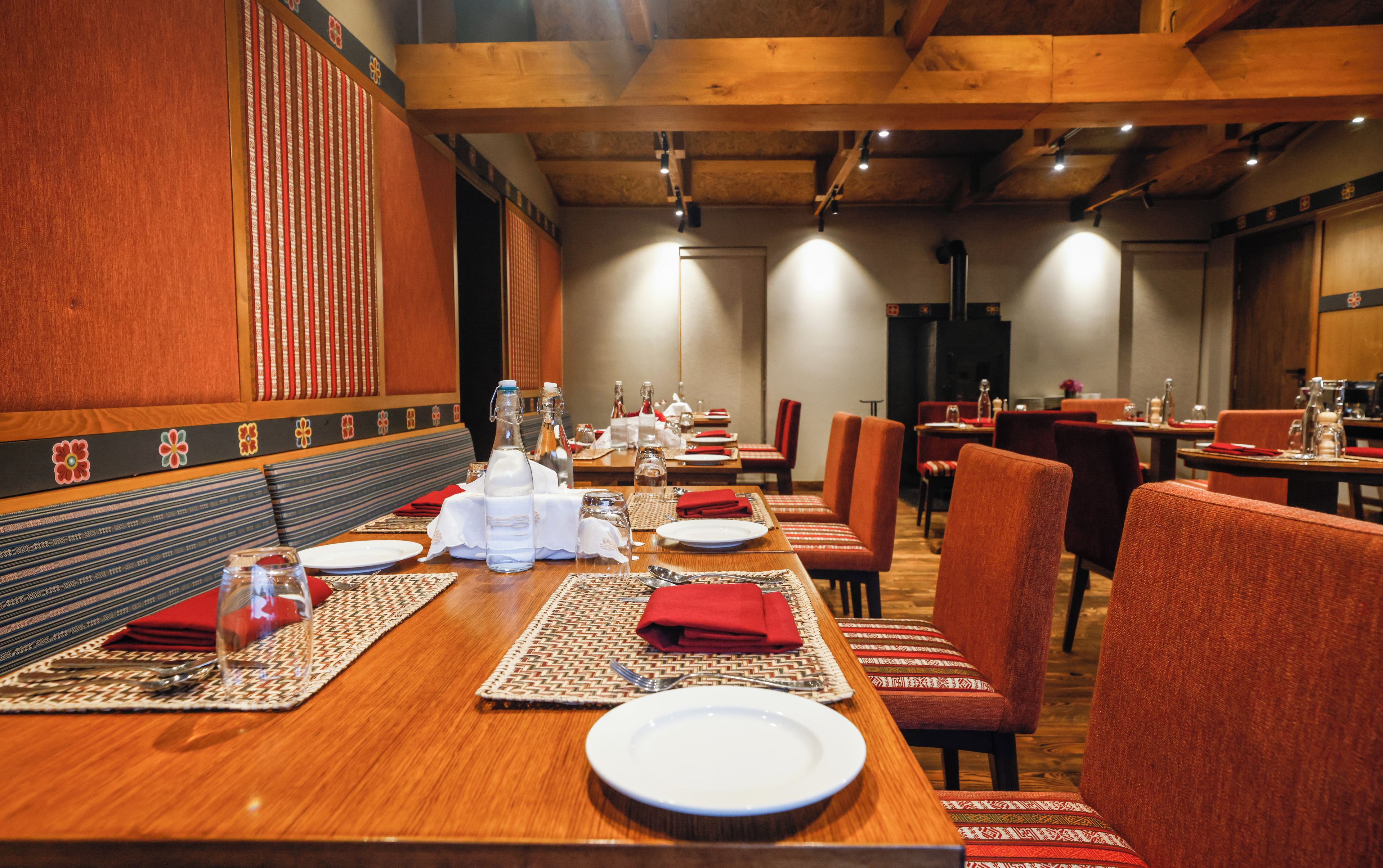 A restaurant with wooden tables, red upholstered chairs, and a patterned wall.