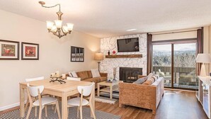 A living room with a fireplace, a dining area, and a balcony with a view. - 2-bedroom 2 bath condo in Winter Park, magnificent views, hot tub, close to town (Winter Park)