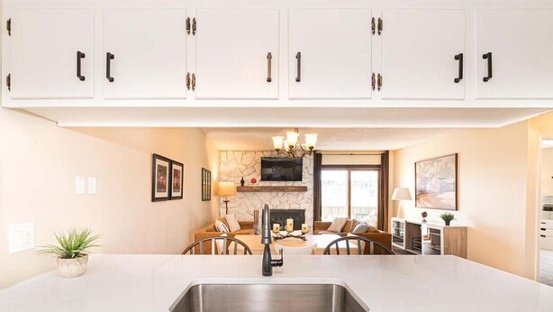 A modern kitchen with white cabinets, a stainless steel sink, and a dining area with a fireplace. - 2-bedroom 2 bath condo in Winter Park, magnificent views, hot tub, close to town (Winter Park)