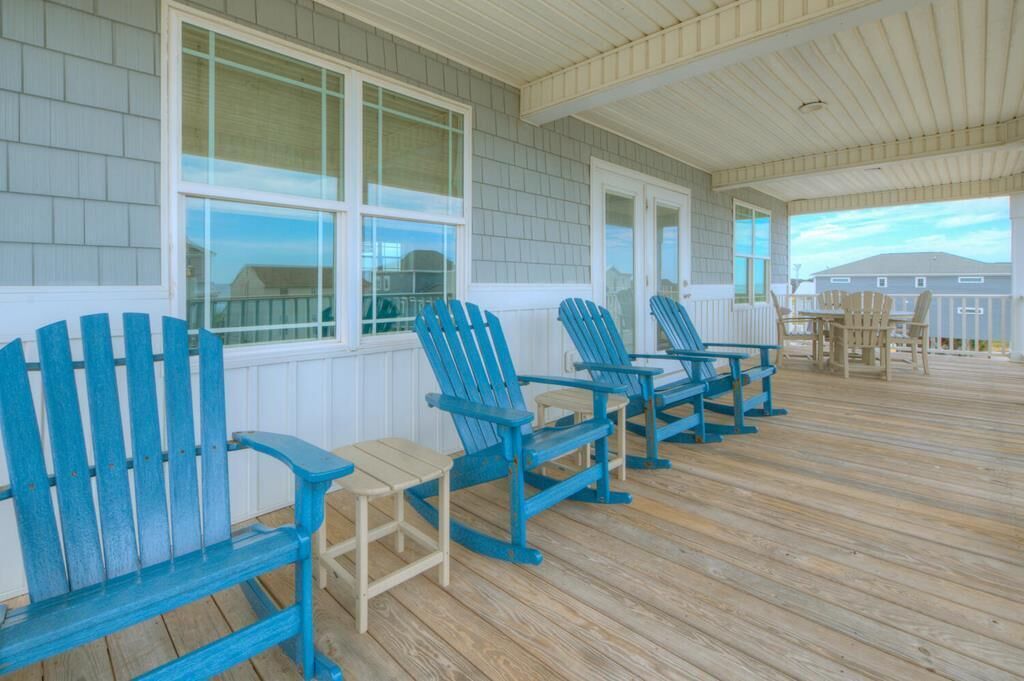 Een overdekt terras met houten vloer en blauwe Adirondack-stoelen.