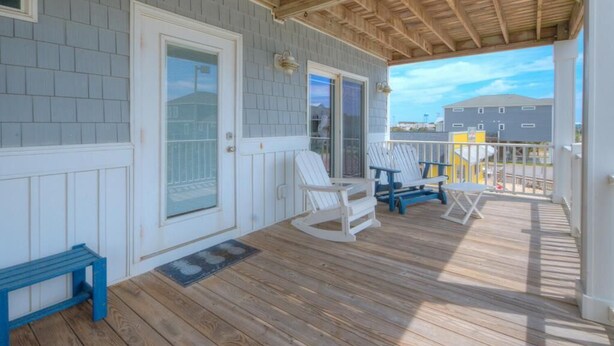 A covered porch with a wooden deck, white rocking chairs, and a blue bench. - Oceanview retreat in Oak Island with private pool, perfect for 11 guests. (Oak Island)
