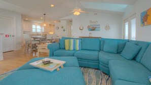 A spacious living room with a teal sofa, a dining area, and a kitchen in the background. - Oceanview retreat in Oak Island with private pool, perfect for 11 guests. (Oak Island)