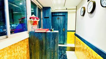 A hotel reception area with a reception desk, a clock, and a sign indicating check-out times.