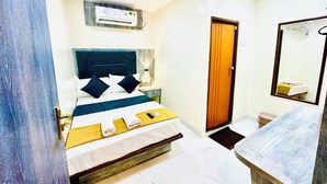 A hotel room with a bed, bedside table, lamp, air conditioning unit, and a bathroom with a mirror and sink. - Hotel BKC Fortune  (Mumbai)