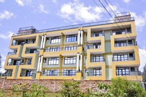 A multi-story building with balconies and windows, featuring a yellow facade and a stone base.
