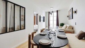 A modern dining room with a round table set for six, a sofa, and a large window with curtains.