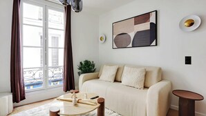 A modern living room with a sofa, a small round table, a potted plant, and a window with curtains.