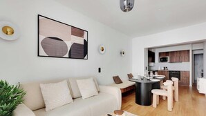 A modern living room with a beige sofa, a round coffee table, and a dining area with a black table and white chairs.
