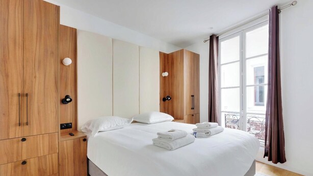 A modern hotel room with a large bed, wooden wardrobe, and a balcony with curtains.
