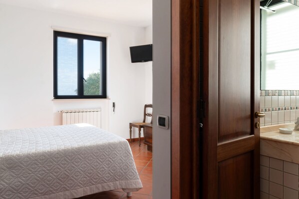 Un dormitorio con cama, ventana, silla y baño con lavamanos y espejo.