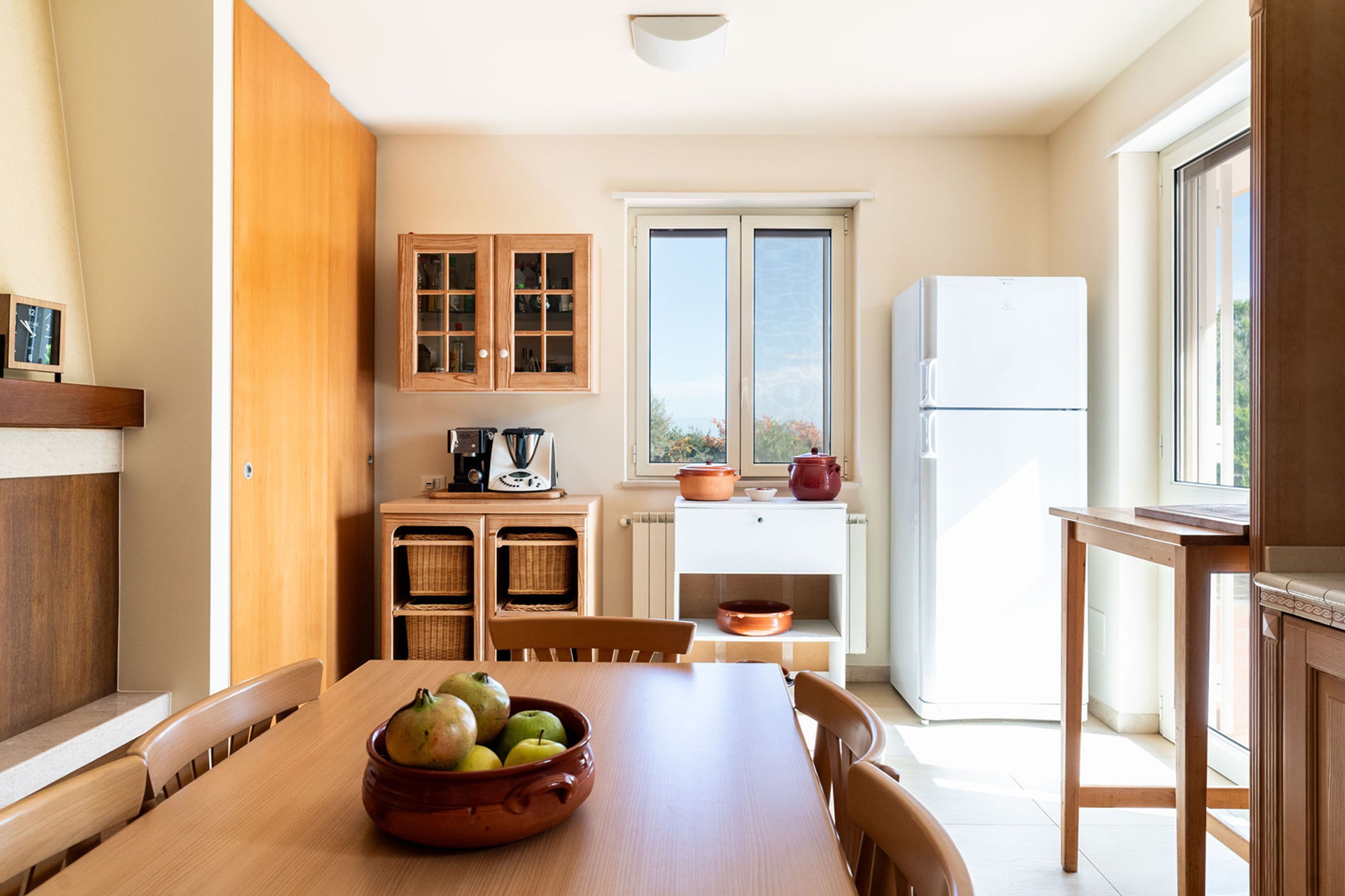 A kitchen with a dining table, wooden cabinets, a refrigerator, and a window with a view.