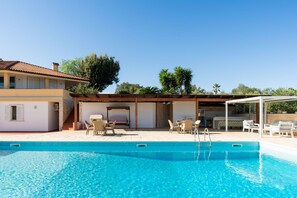 Una piscina con sillones de descanso y un área de terraza cubierta.