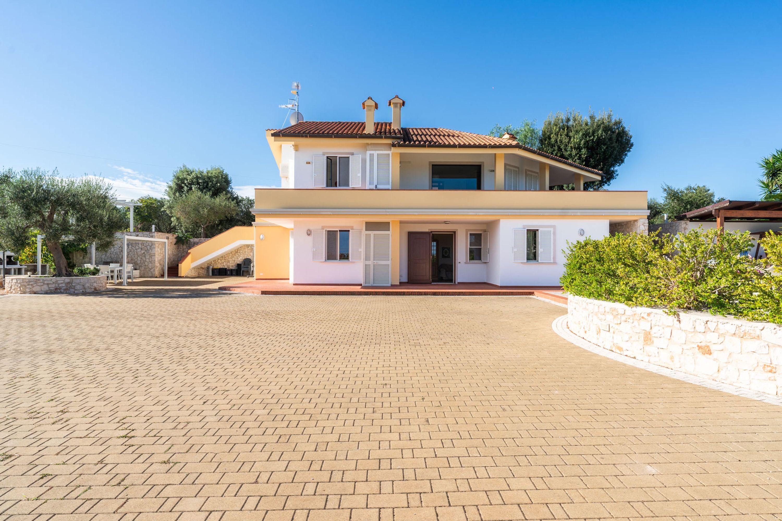 A two-story house with a paved driveway, a stone wall, and a small garden area.