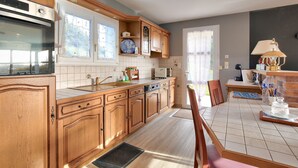 Una cocina con armarios de madera, horno empotrado, lavamanos y comedor con mesa y sillas.