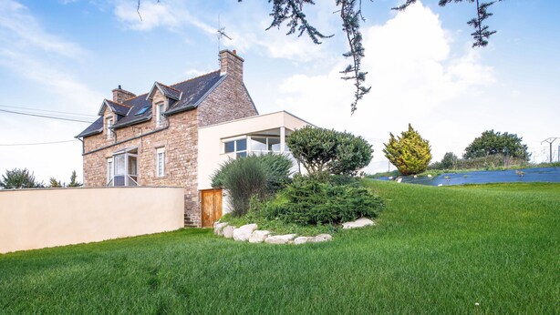 Una casa de dos pisos con fachada de piedra y una extensión moderna.