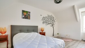 Un dormitorio con una cama grande, cabecera, un mural en la pared, una mesita de noche y una mesita auxiliar.