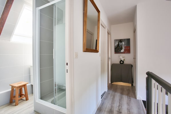 A hallway with a wooden stool, a glass shower door, a mirror, and a painting on the wall. - House for 6 with large garden & BBQ – Erquy (Erquy)