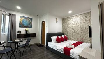 A modern hotel room with a bed, a desk, a chair, a small table, and a painting on the wall.