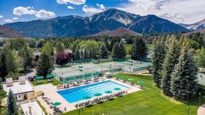 Een resort met een zwembad, tennisbanen en een bergachtig landschap op de achtergrond.