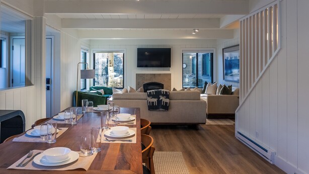Een ruime woonkamer met een houten eettafel voor vier personen, een bank en een open haard.