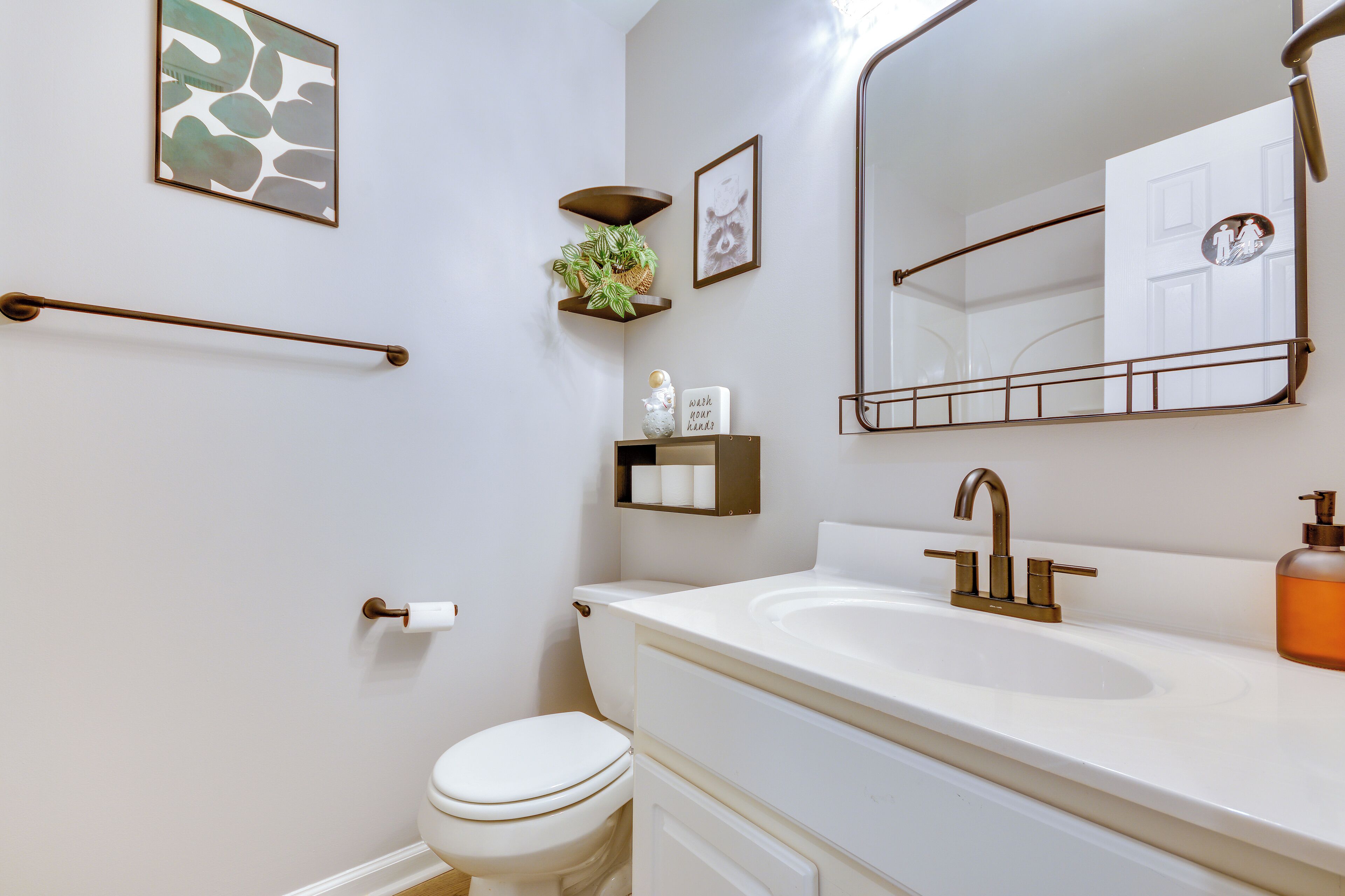 A modern bathroom with a white sink, gold faucet, and a large mirror.
