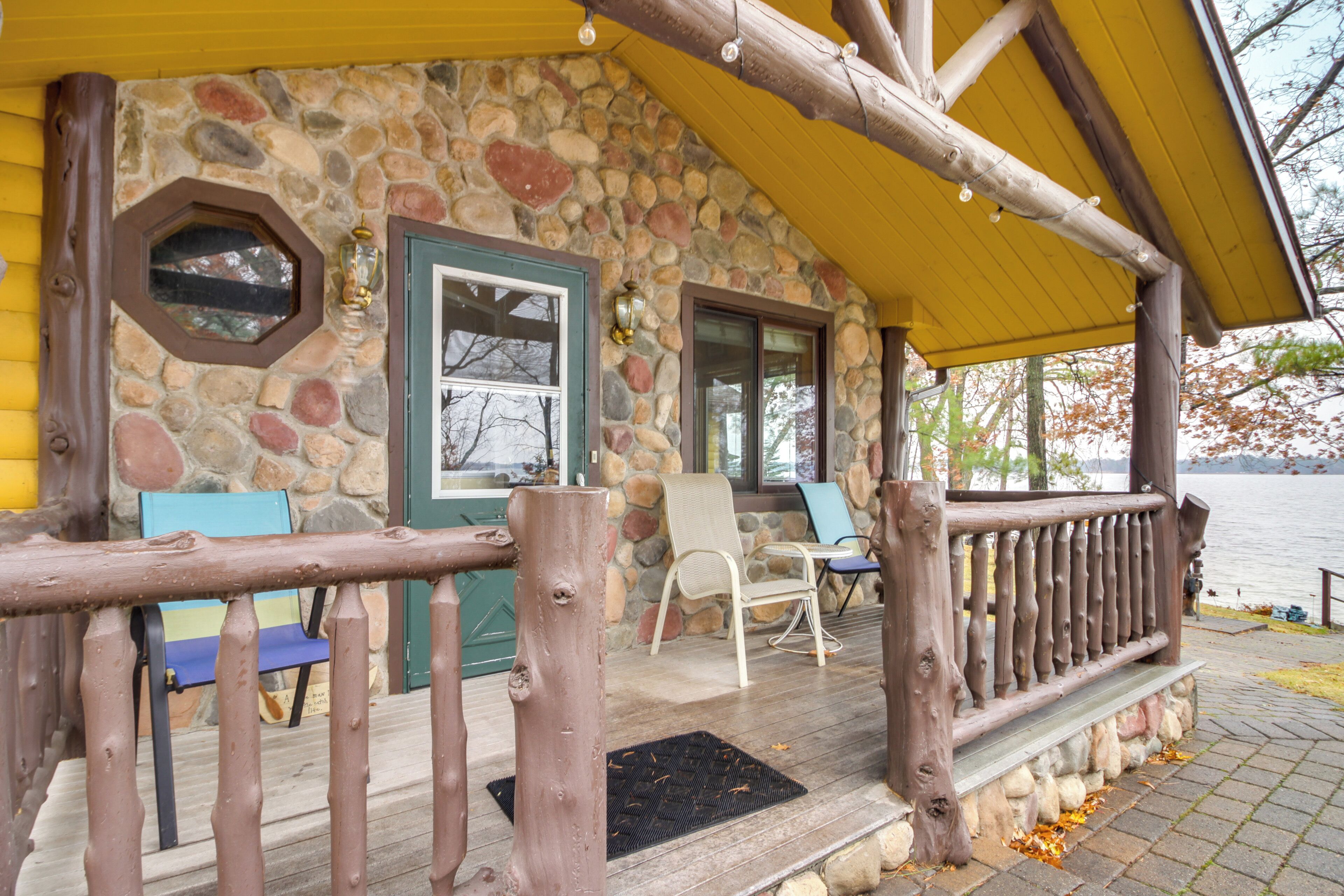 A stone cabin with a wooden porch, a bench, and a view of a lake.