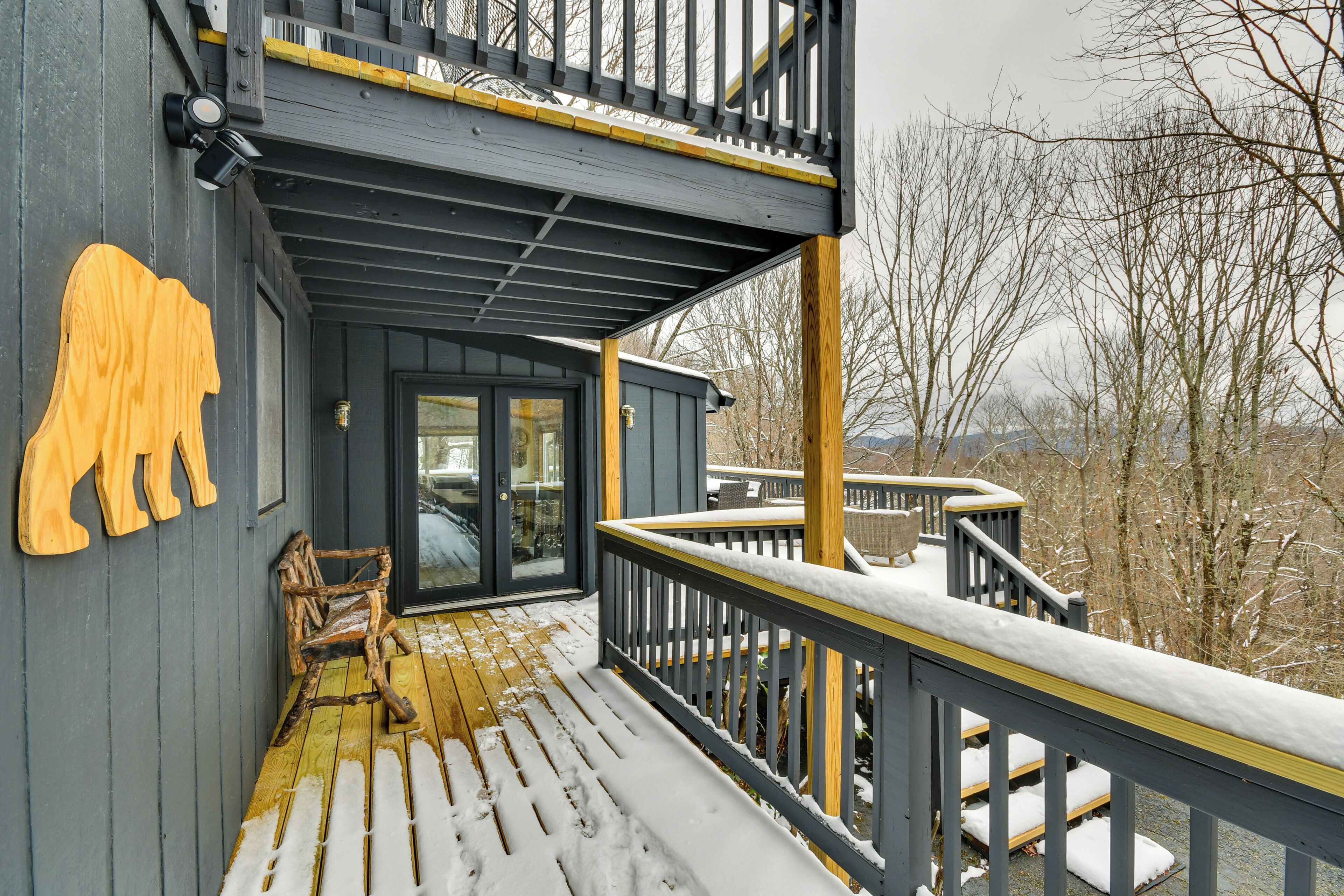 Une terrasse en bois, avec de la neige sur les rampes et les marches, un banc et une porte vitrée donnant sur un espace abrité.