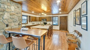 A modern kitchen with a stone wall, wooden ceiling, and a central island with bar stools. - 6 Mi to Skiing! Hot Tub Hideaway in Seven Devils (Banner Elk)