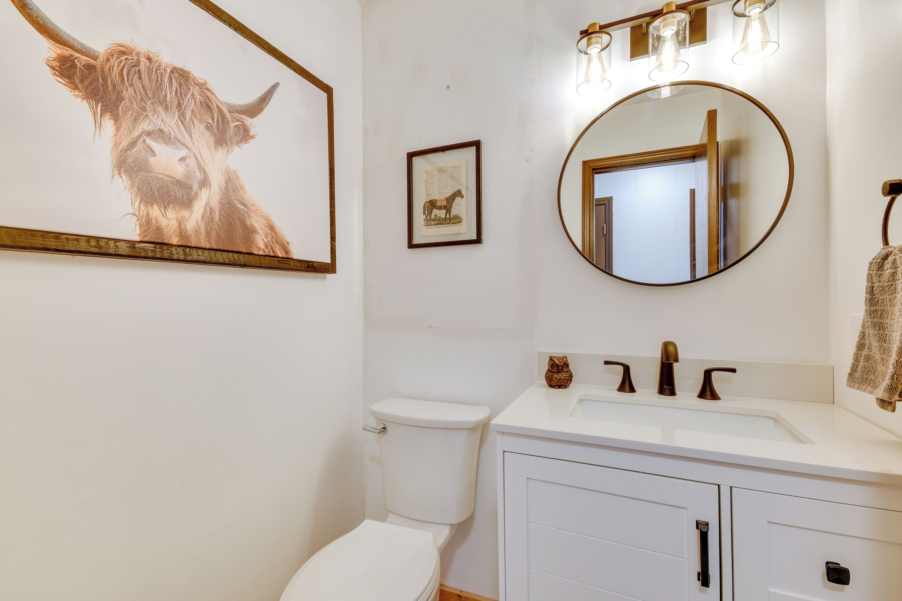 Un baño con inodoro blanco, un lavamanos con espejo y un cuadro de un caballo en la pared.