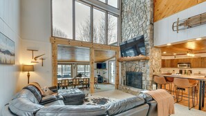 A spacious living area with a leather sofa, a stone fireplace, and a kitchen with bar stools. - 6 Mi to Skiing! Hot Tub Hideaway in Seven Devils (Banner Elk)