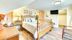 A bedroom with a wooden bed, bedside tables, a lamp, and a flat-screen TV mounted on the wall.