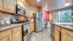A modern kitchen with wooden cabinets, stainless steel appliances, granite countertops, and a red accent wall. - Mtns Await: Reno Escape w/ Yard & Pool Table! (Reno)