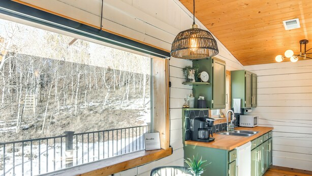 A cabin interior with a dining area, kitchen, and a view of a snowy forest. - Mtn-view Haven w/ Hot Tub: 9 Mi to Dtwn Bailey (Bailey)