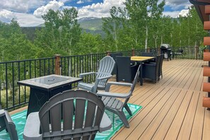 Una terraza con mobiliario exterior, incluyendo sillas y una mesa, con vista a una zona boscosa y montañas distantes.