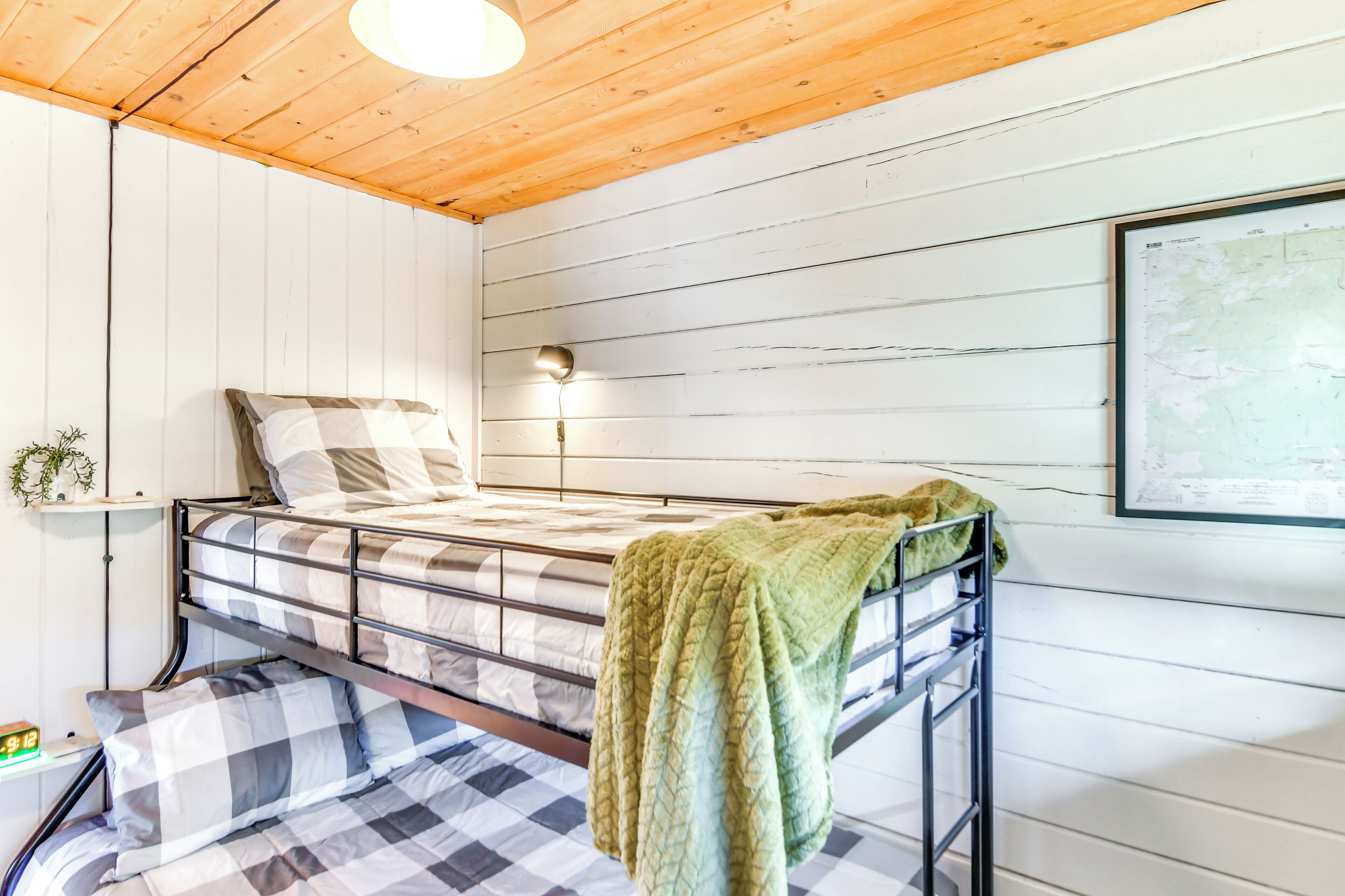 A bunk bed with a green blanket, a bedside lamp, a map on the wall, and a small plant on a shelf.