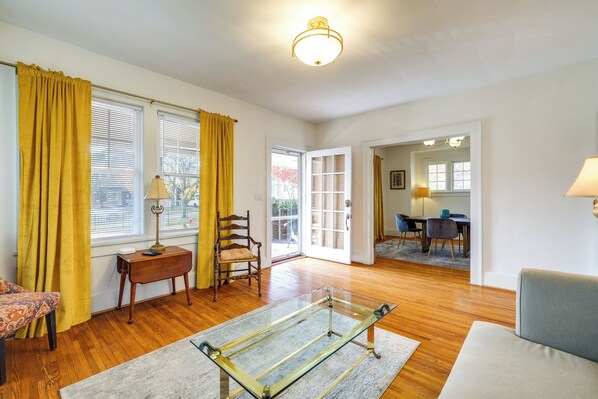 A spacious living room with hardwood floors, a glass coffee table, a sofa, and a dining area with a table and chairs. - Walk to The Grandin Theatre: Roanoke Unit w/ Yard! (Roanoke)