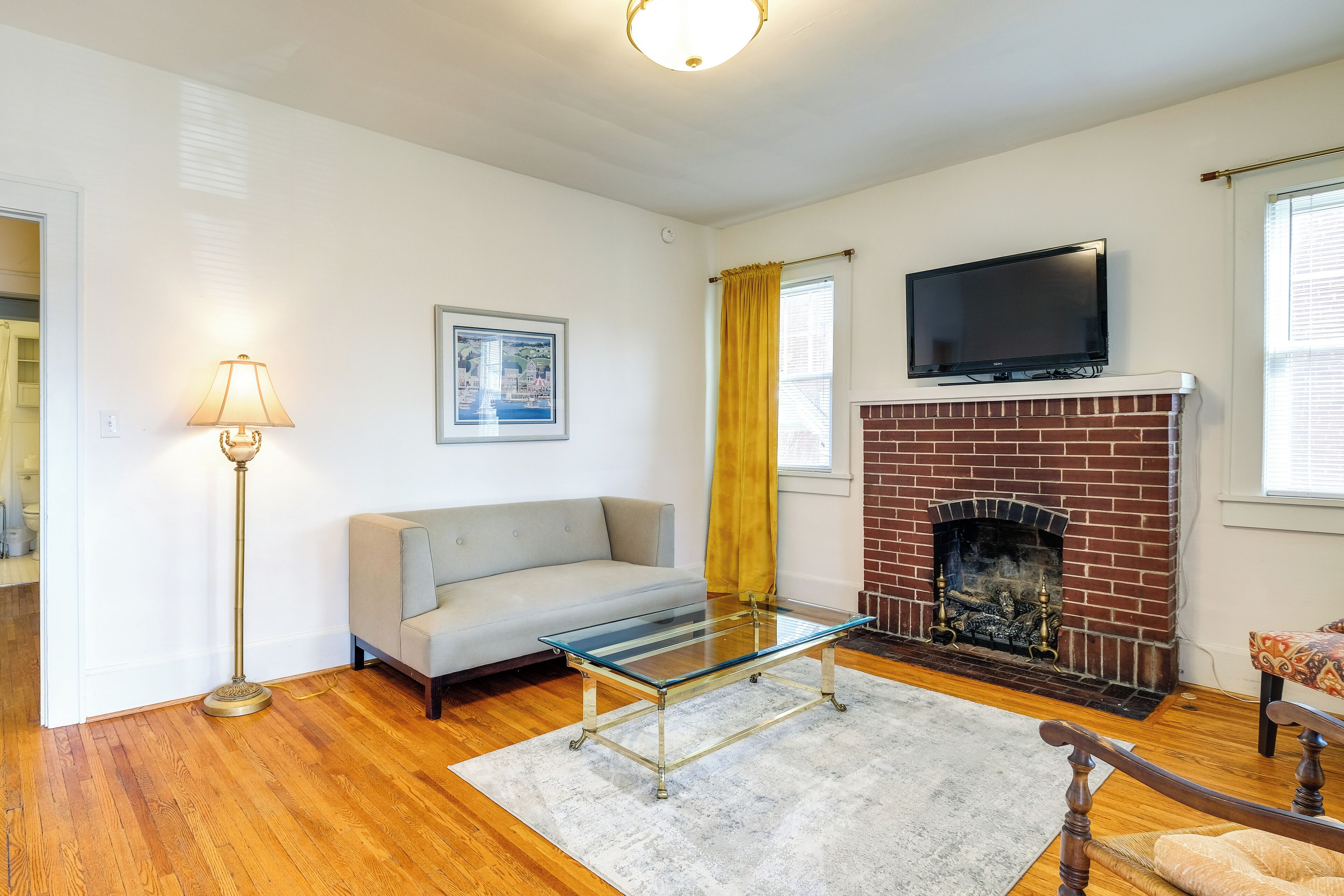 A living room with a sofa, a glass coffee table, a fireplace, and a television mounted above it.