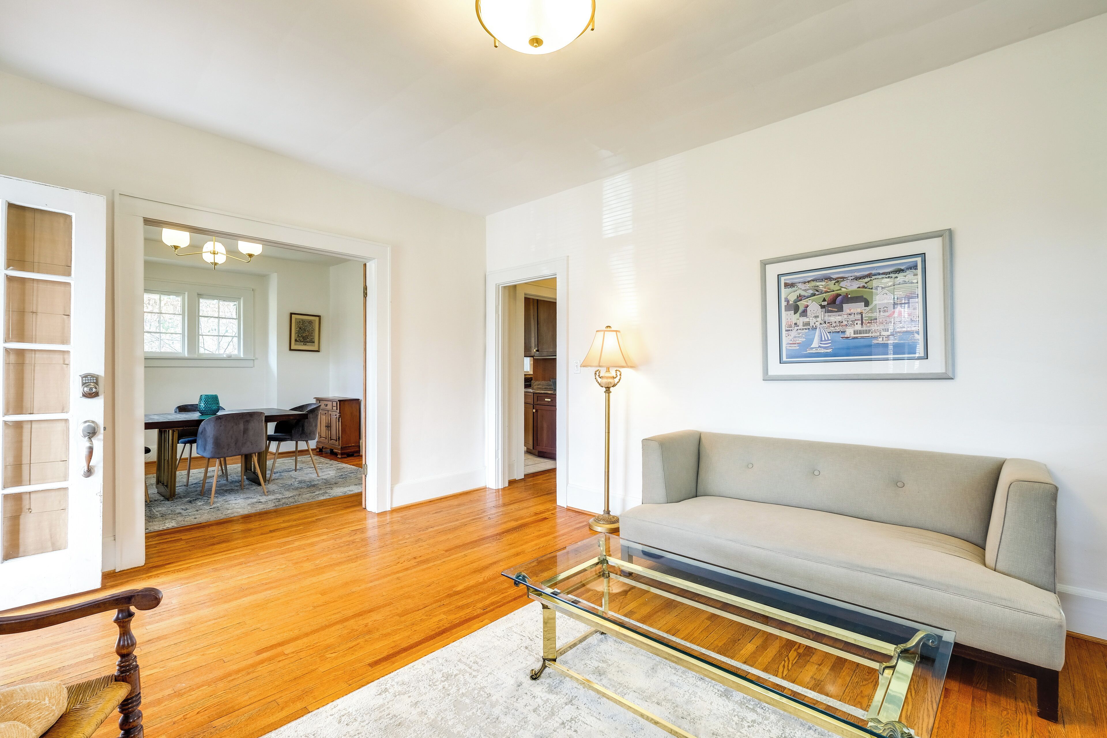 A living room with a sofa, a glass coffee table, a lamp, and a dining area with a table and chairs.